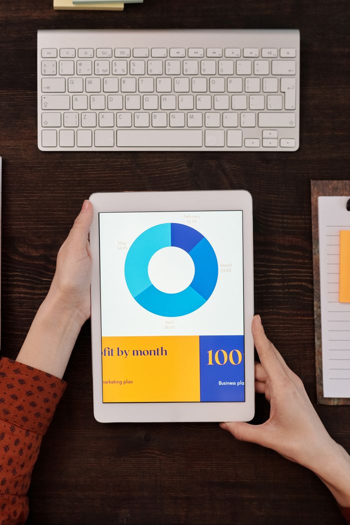 ours-journey A person holds a tablet showing a business graph next to a keyboard on a wooden desk.
